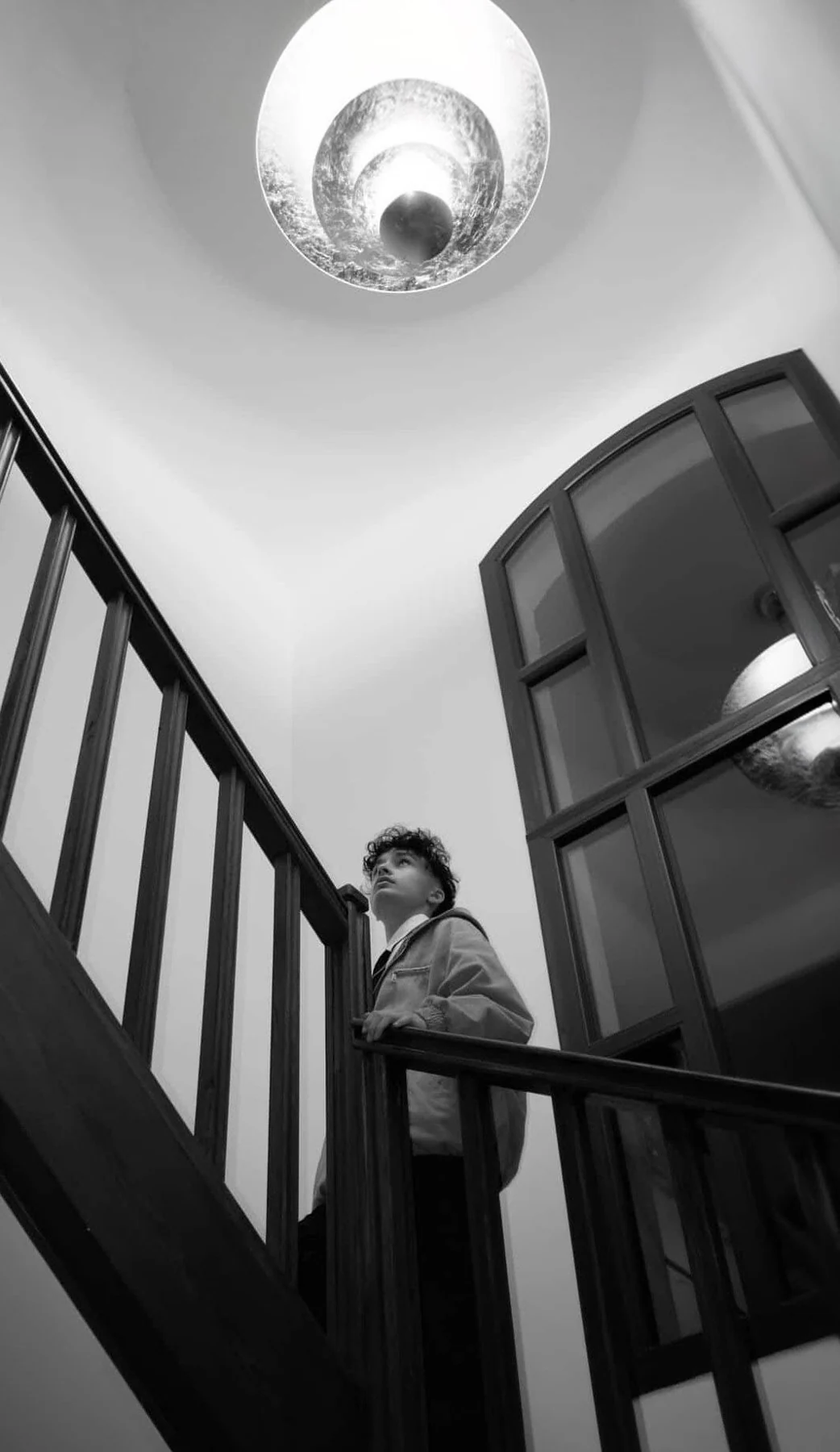 Portrait en noir et blanc d’Axel dans un escalier, sous un luminaire, photographié en tant que mannequin.