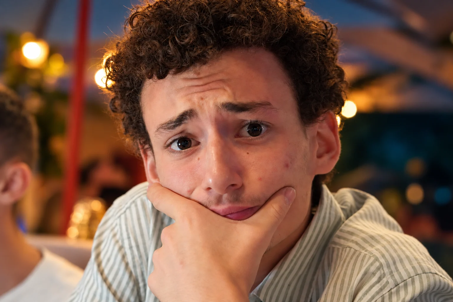 Portrait d’un homme aux cheveux bouclés, le menton posé dans sa main, dans une lumière chaleureuse.