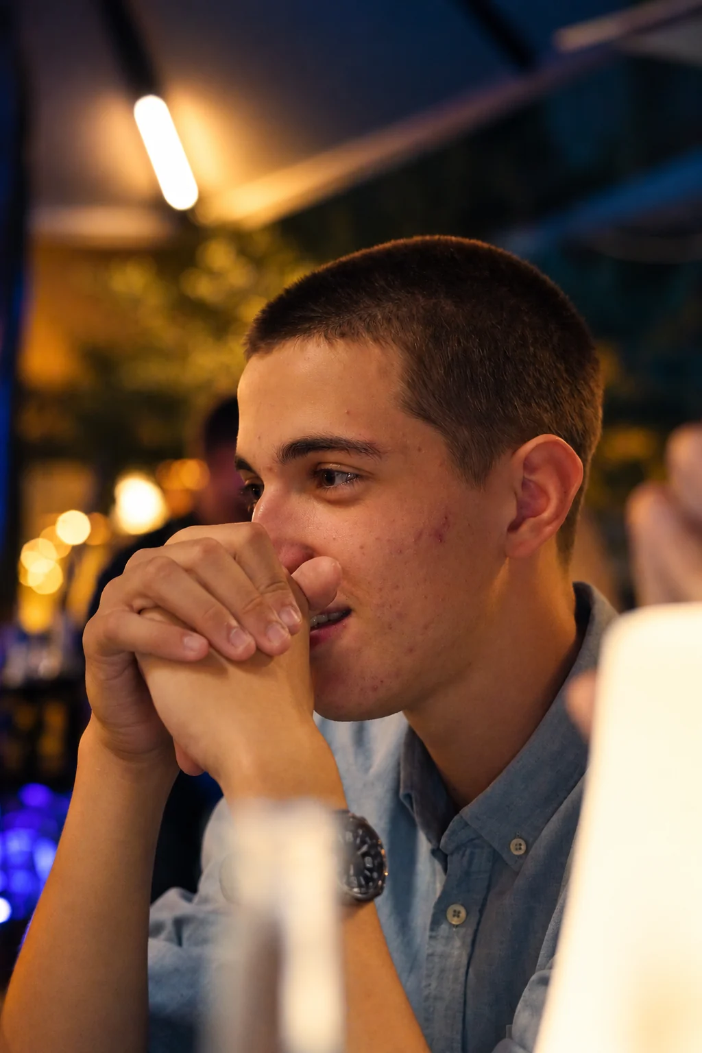 Un homme en chemise bleue sourit derrière ses mains, série flo.