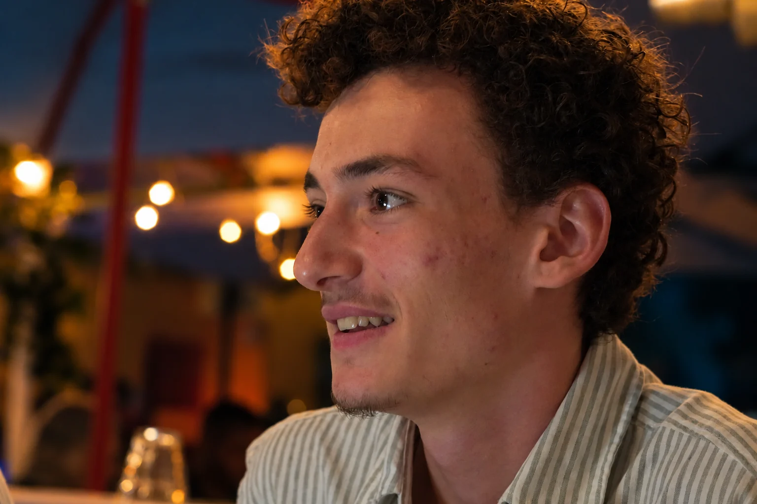 Portrait de profil d’un homme aux cheveux bouclés et au sourire spontané, série flo.