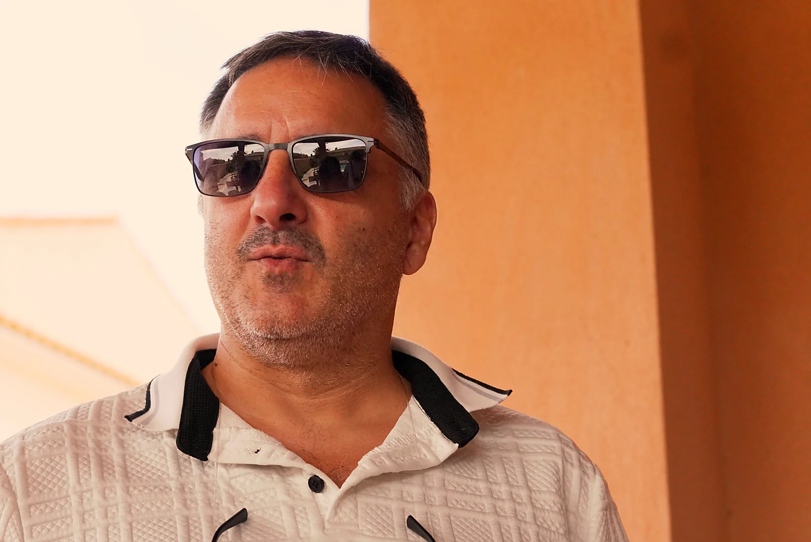 Portrait d’un homme en lunettes de soleil et polo clair à la crémaillère de Leslie.